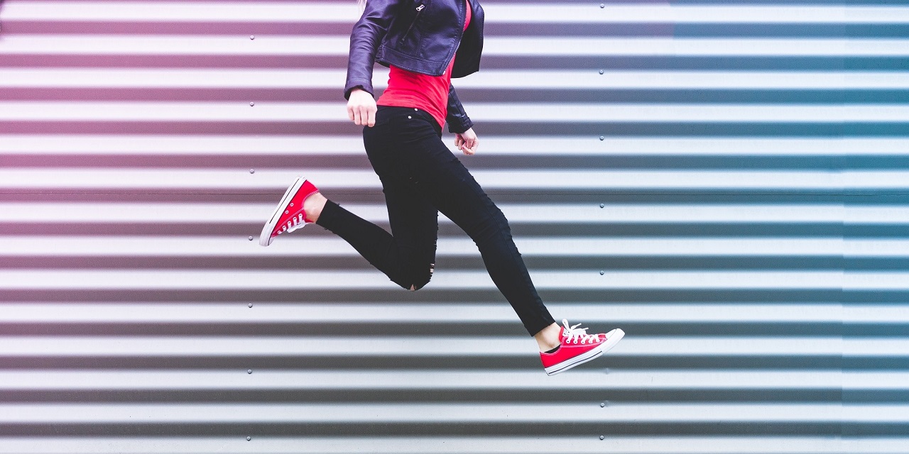 Springende, junge Frau mit roten Converse Schuhen